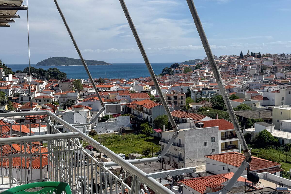 A coastal cityscape with red-tiled rooftops, a view of the sea, and a bridge in the foreground.