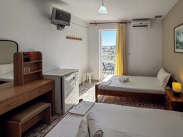 Habitación de hotel con cama, escritorio, televisión, aire acondicionado y vista a la ciudad desde la ventana.