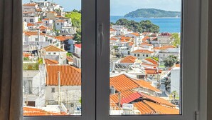 A room with a bed, a window, and a view of a coastal town with red-roofed buildings. - Skiathos Platis House (Skiathos)