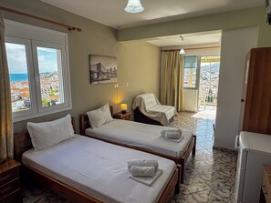 A hotel room with two beds, a small table, a lamp, and a view of the city. - Skiathos Platis House (Skiathos)