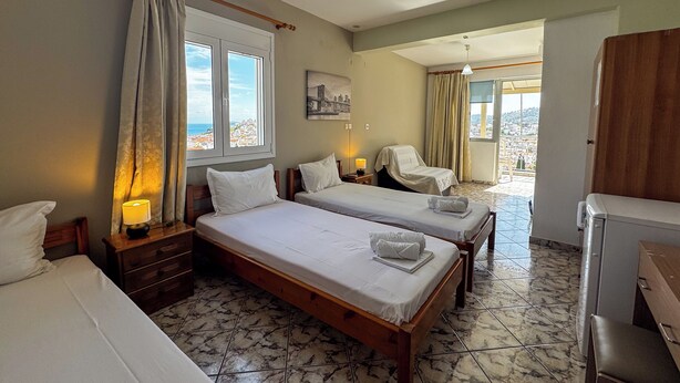 A hotel room with two beds, a chair, a desk, and a view of the city. - Skiathos Platis House (Skiathos)