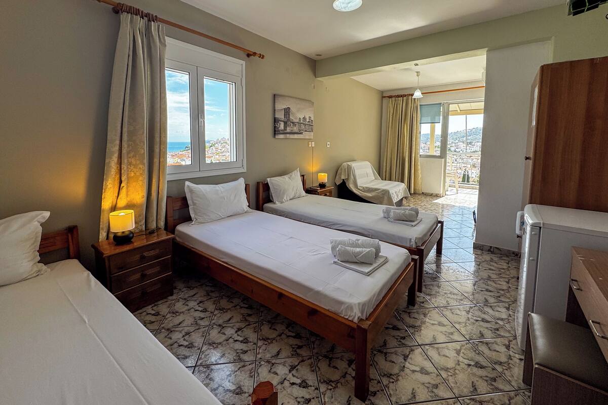 A hotel room with two beds, a chair, a desk, and a view of the city.