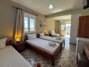 A hotel room with two beds, a chair, a desk, and a view of the city. - Skiathos Platis House (Skiathos)