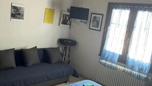 Une pièce comprenant un canapé, un lit, un téléviseur fixé au mur et une fenêtre avec des rideaux.