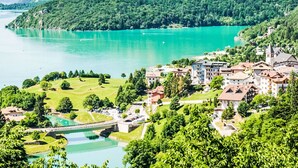 A lakeside town with buildings, a bridge, and lush greenery.