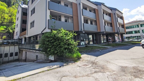 A multi-story building with balconies, a parking area, and a small garden.