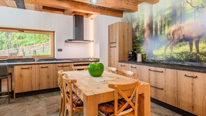 Una cocina moderna con armarios de madera, una mesa de comedor y sillas. Se observa un ventanal con vistas al bosque.