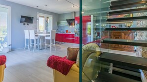 Un soggiorno moderno con una parete divisoria in vetro, un divano e un'area da pranzo con sedie bianche.