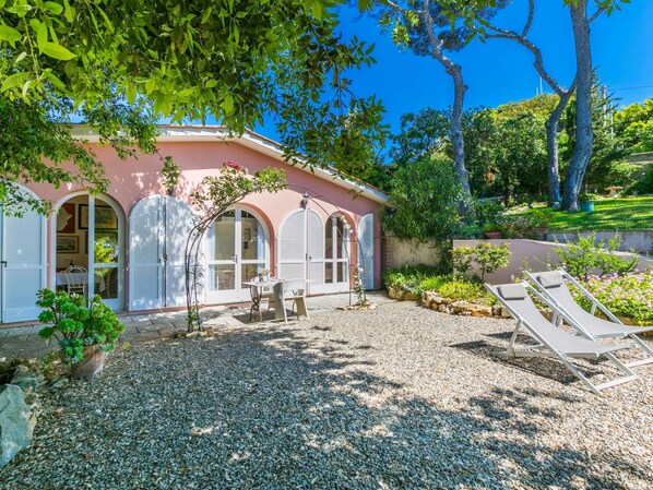 Een roze villa met een terras van grind, buitenmeubels en een tuin.