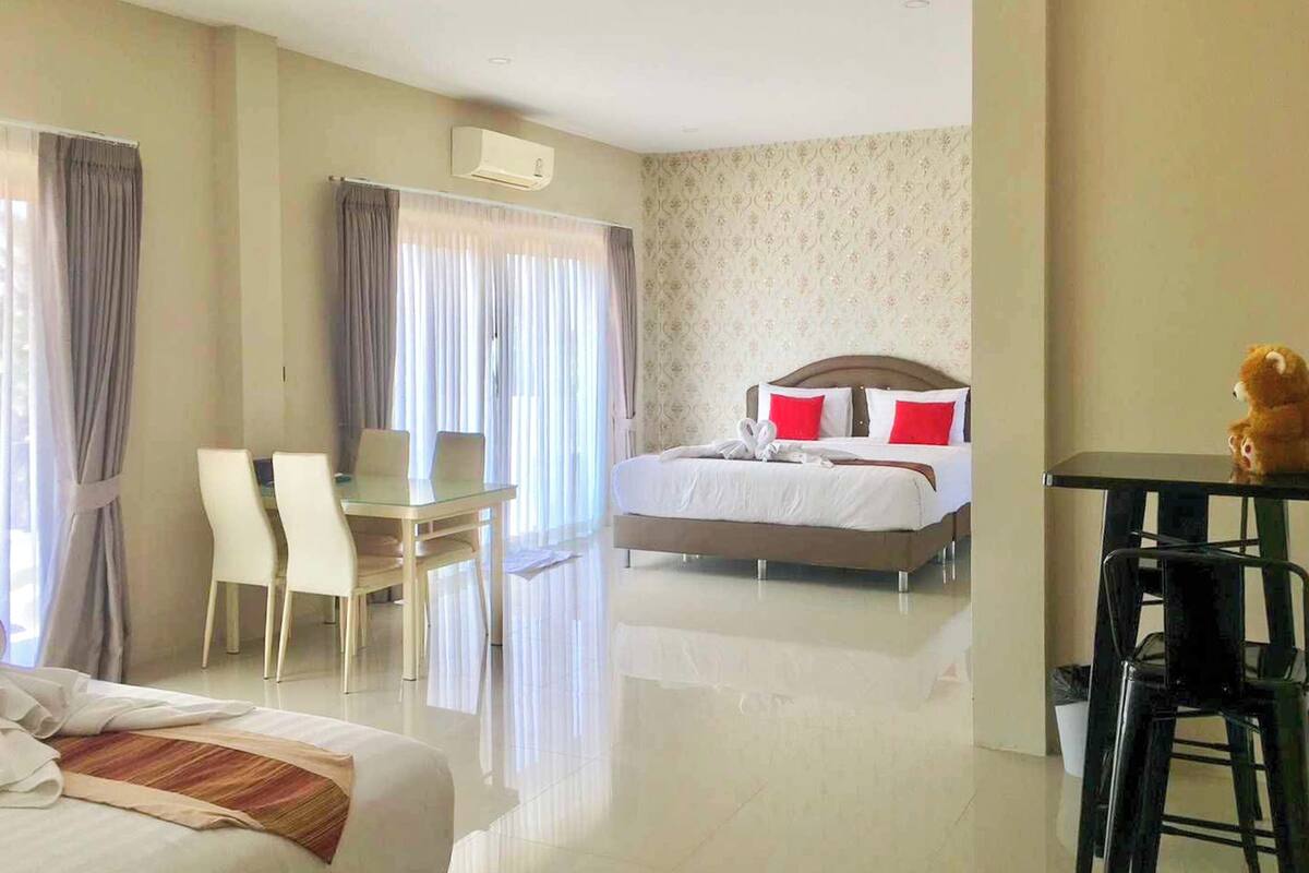 A hotel room with a bed, a desk, two chairs, a small table, and a teddy bear.
