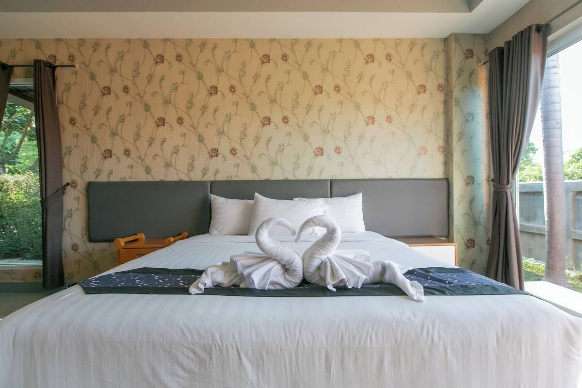 A hotel room with a large bed, floral wallpaper, and a view of greenery outside.