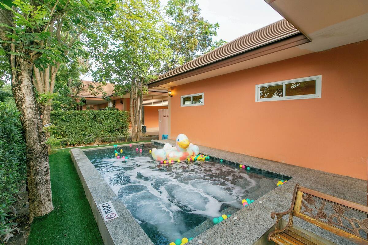 A swimming pool with a duck floatation device, surrounded by greenery and a building with a peach-colored exterior.
