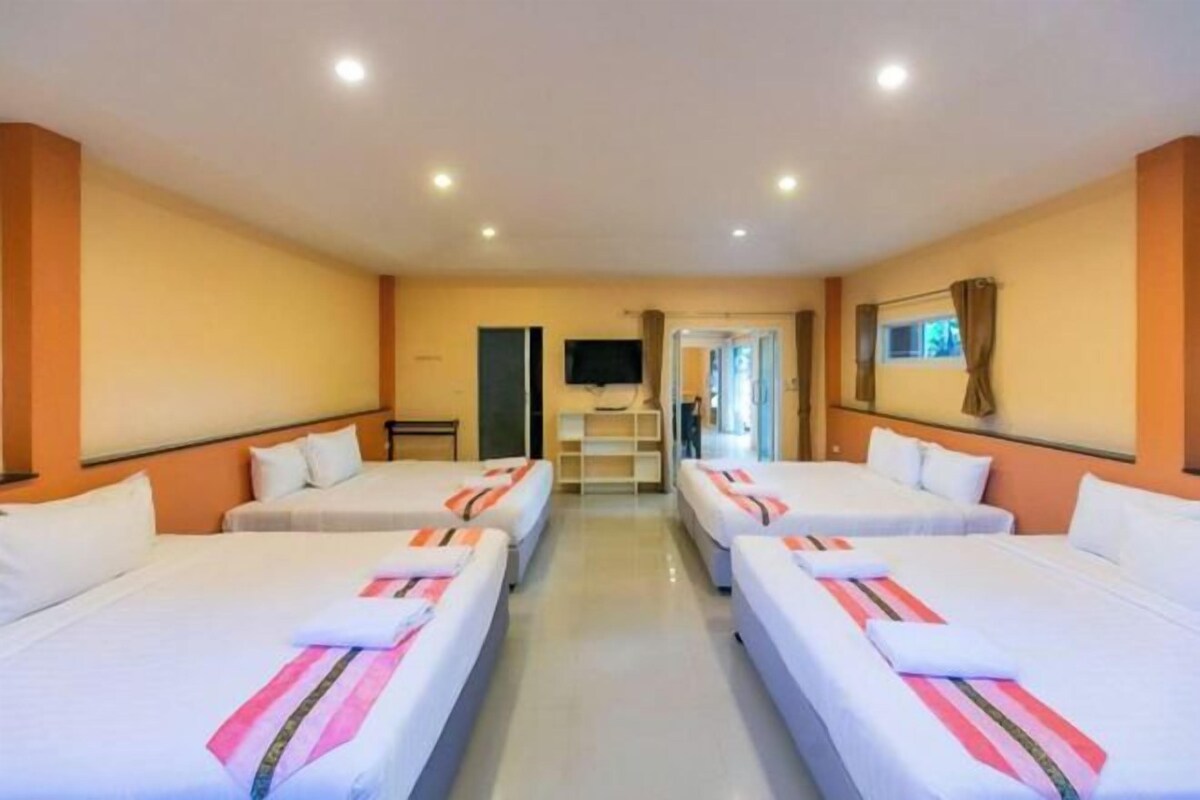 A hotel room with four single beds arranged in a row, a flat-screen TV mounted on the wall, and a small table with a chair.