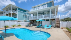 A two-story house with a swimming pool, outdoor furniture, and a white fence.