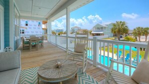A covered outdoor area with a wooden deck, white railings, and a view of a swimming pool and neighboring houses.