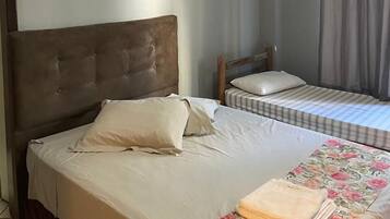 A bedroom with a large bed, a smaller bed, a headboard, a pillow, a blanket, a framed picture on the wall, and a curtain.