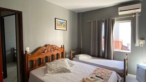 Un dormitorio con dos camas, ventilador de techo, aire acondicionado, ventana con cortinas e imagen enmarcada en la pared.
