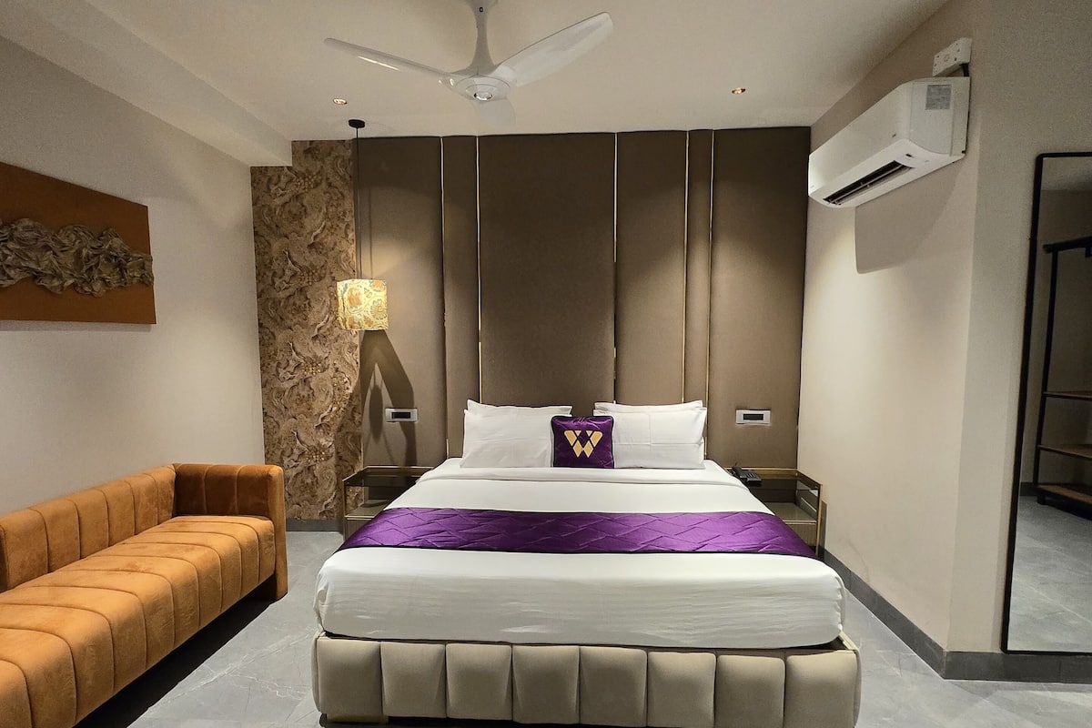 Un dormitorio moderno con una cama grande, un sofá, un ventilador de techo y un equipo de aire acondicionado.