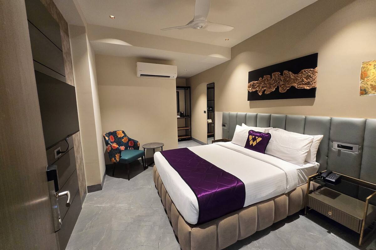 Habitación de hotel moderna con una cama grande, una silla, una mesita pequeña, una mesita de noche y un ventilador de techo.