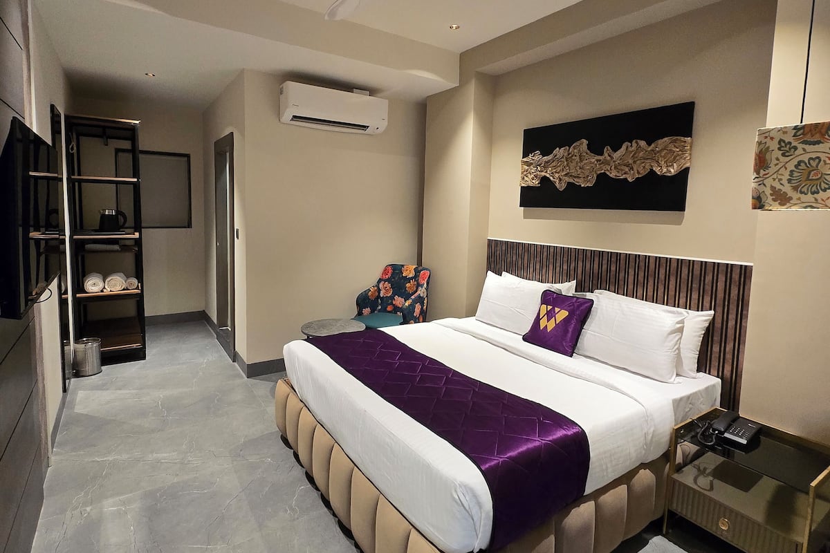 Una habitación de hotel moderna con una cama grande, un ventilador de techo, un equipo de aire acondicionado, una mesita auxiliar pequeña y un televisor.
