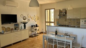 Una cocina moderna con armarios blancos, un comedor con mesa y sillas blancas, y un televisor montado en la pared.