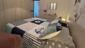 Un dormitorio con una cama grande, una mesita de noche, un aparador, un espejo y una puerta que da a otra habitación.