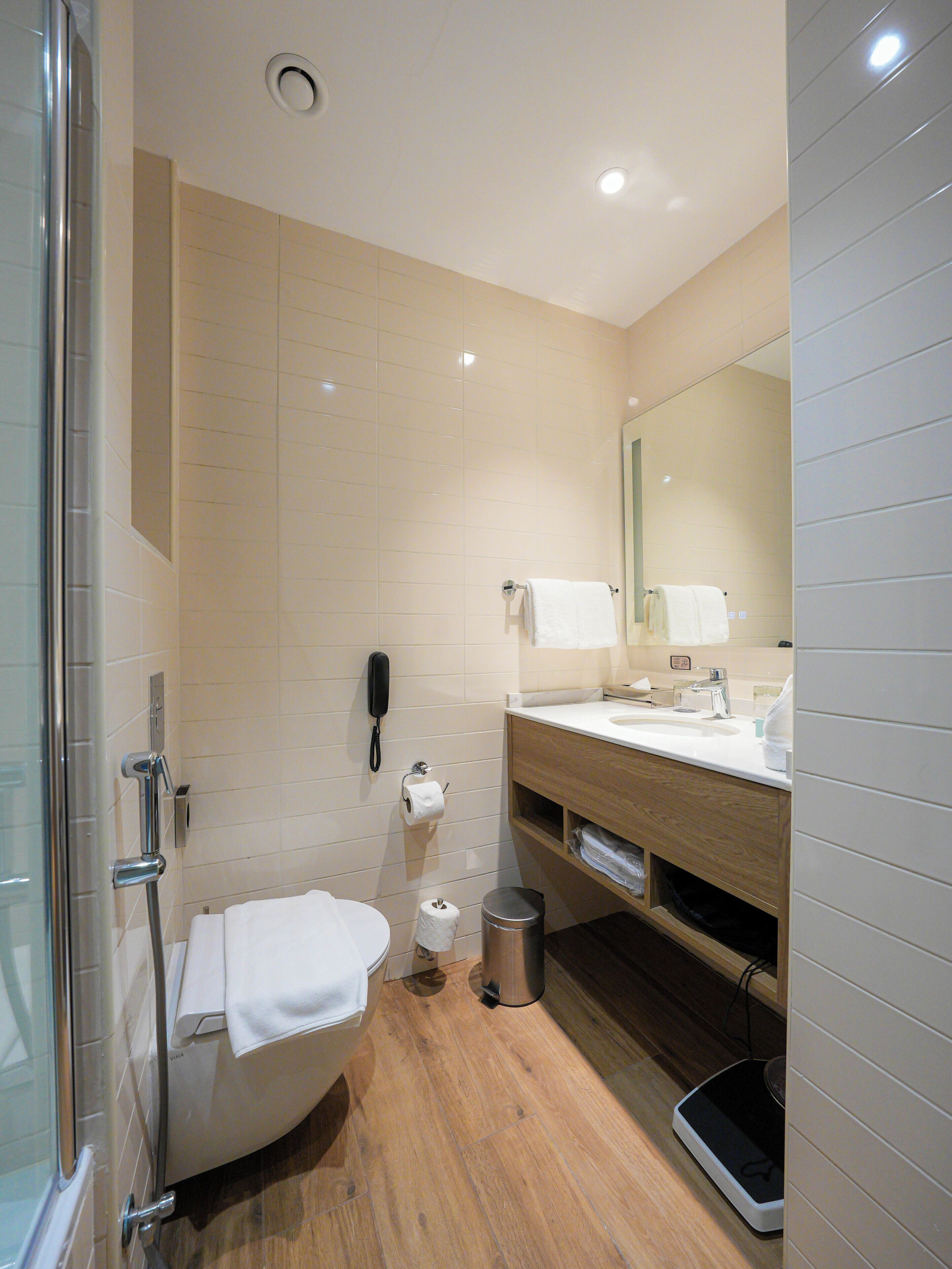 A modern bathroom with a glass shower enclosure, a toilet, a sink with a mirror, and a trash can.