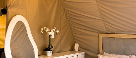 Une pièce aménagée comme une tente, avec un lit, une coiffeuse dotée d’un miroir, une commode et des lampes suspendues.