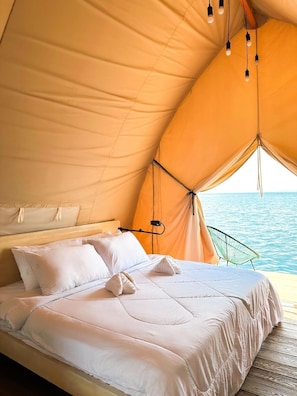 A tented room with a bed, pillows, and a view of the sea.