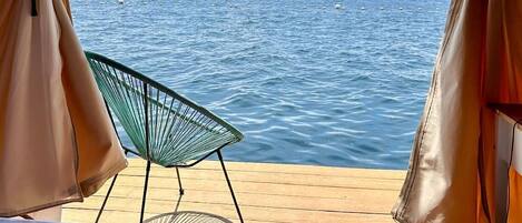 A tent with a view of the sea, a chair, and a bed.