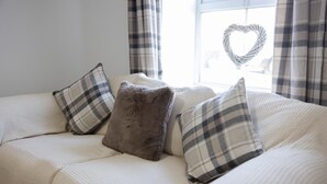 A bed with a white textured cover, two plaid pillows, and a heart-shaped decoration on the window.