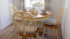 A dining area with a round wooden table, white chairs, and a window with curtains.