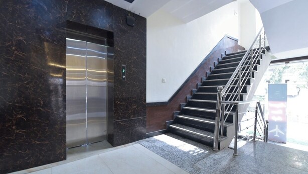 Un ascenseur moderne doté d’un écran numérique, un escalier avec des rampes en métal et un sol carrelé.