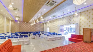 Une salle de conférence avec des rangées de chaises blanches, un canapé rouge et une moquette à motifs.