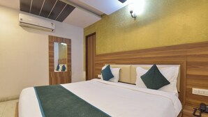 Une chambre d’hôtel comprenant un lit, une table de chevet avec un téléphone, un climatiseur fixé au mur, un miroir et une tête de lit en bois.