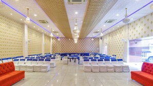 Une salle de conférence avec des rangées de chaises blanches, des canapés rouges et un tapis à motifs.