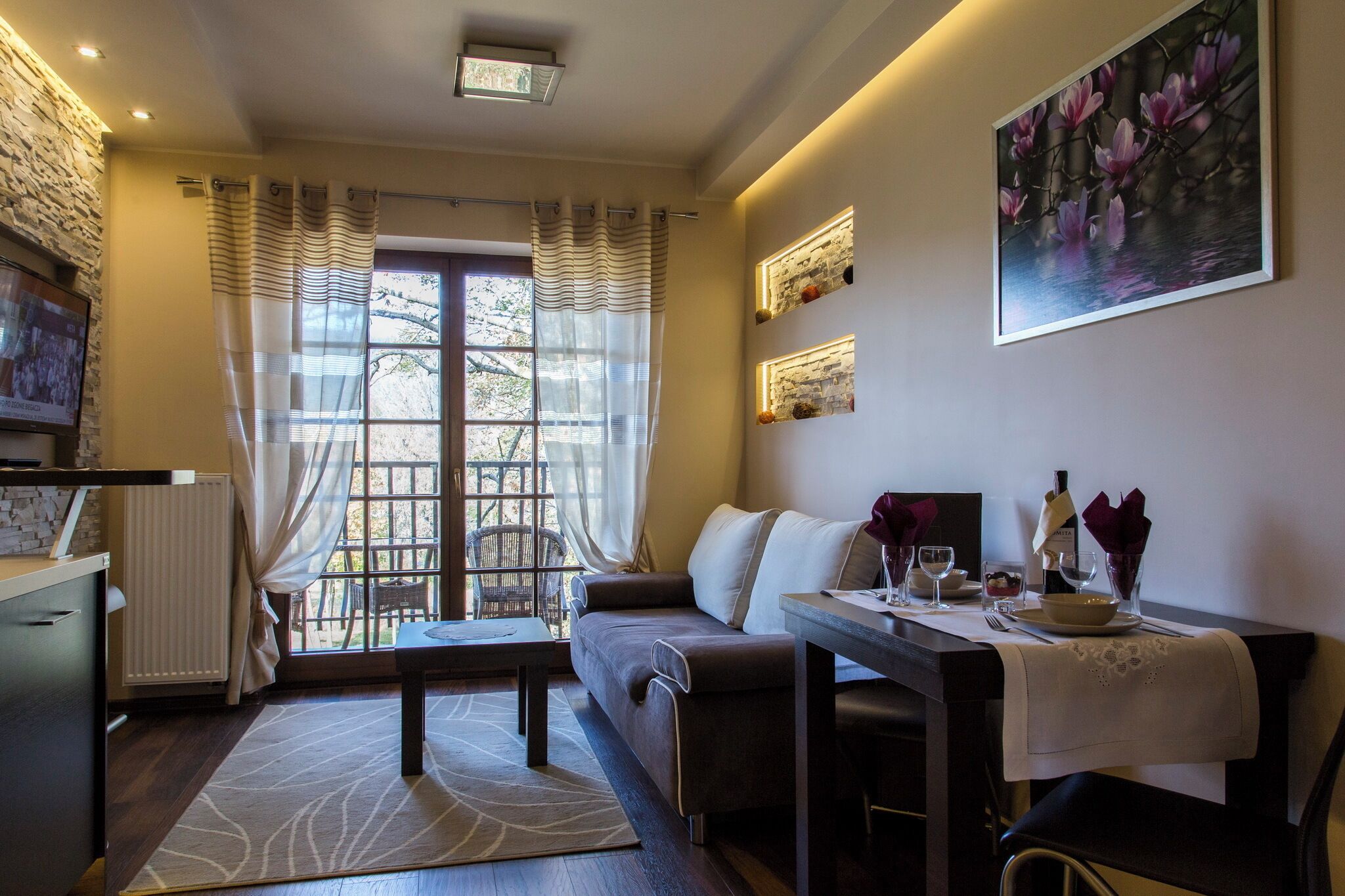 Una sala de estar acogedora con un sofá, una mesa de comedor dispuesta con copas de vino y vistas a través de un amplio ventanal.