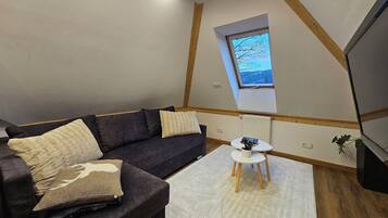 A cozy loft bedroom with a dark brown sofa, a small white table, and a skylight window.