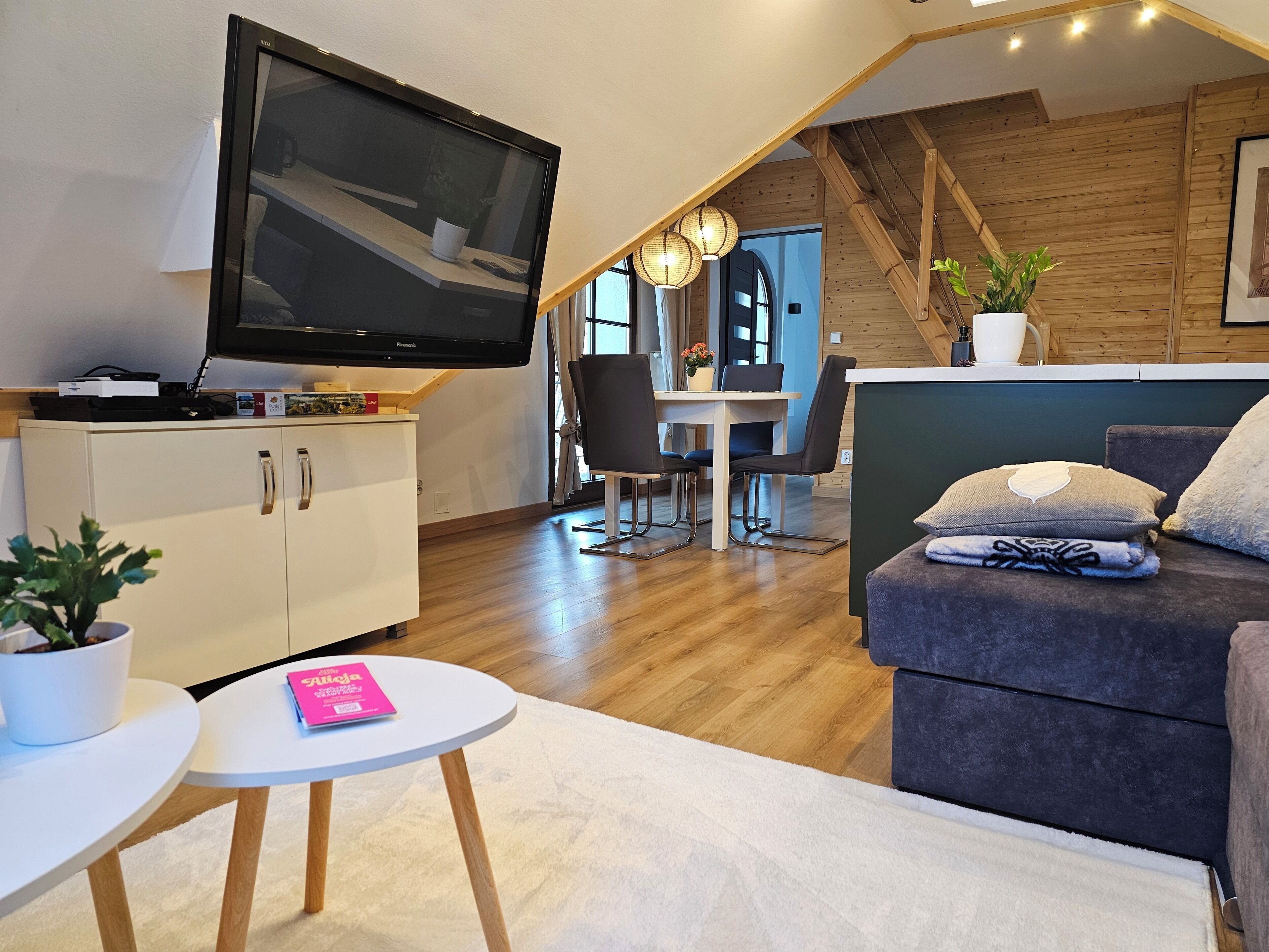 Una sala de estar moderna con televisor de pantalla plana, comedor y una escalera que conduce a un nivel superior.