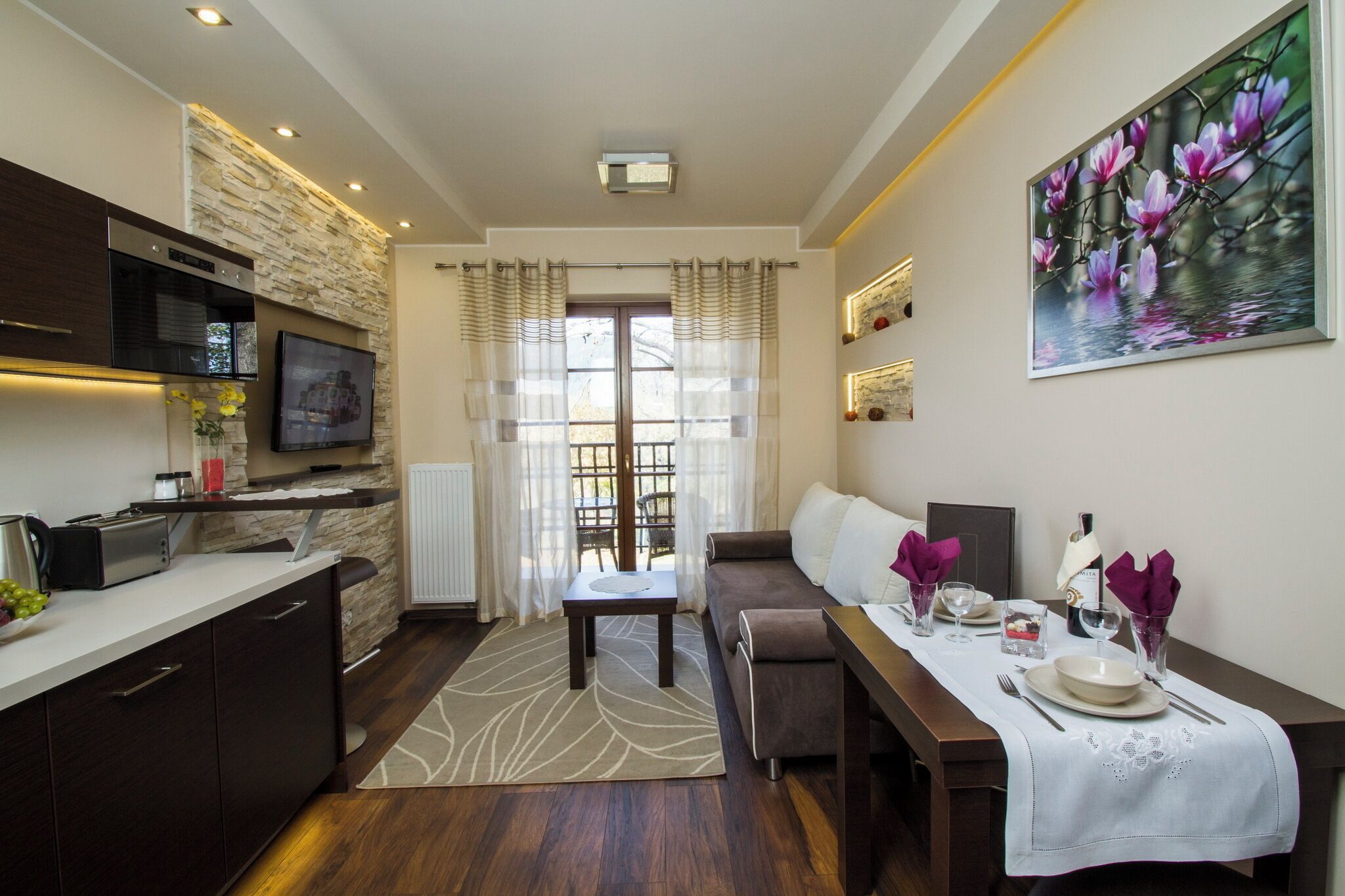 A modern kitchen with a stone accent wall, a dining area with a white tablecloth, and a sofa.