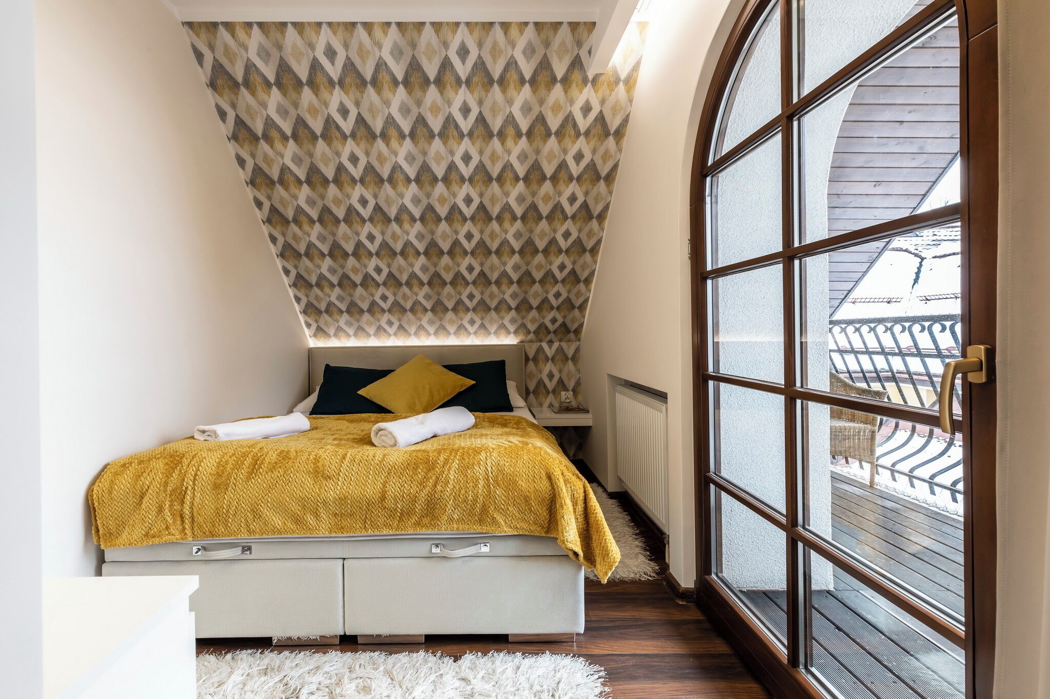 A bedroom with a bed, a patterned ceiling, a large window, and a view of the outside.
