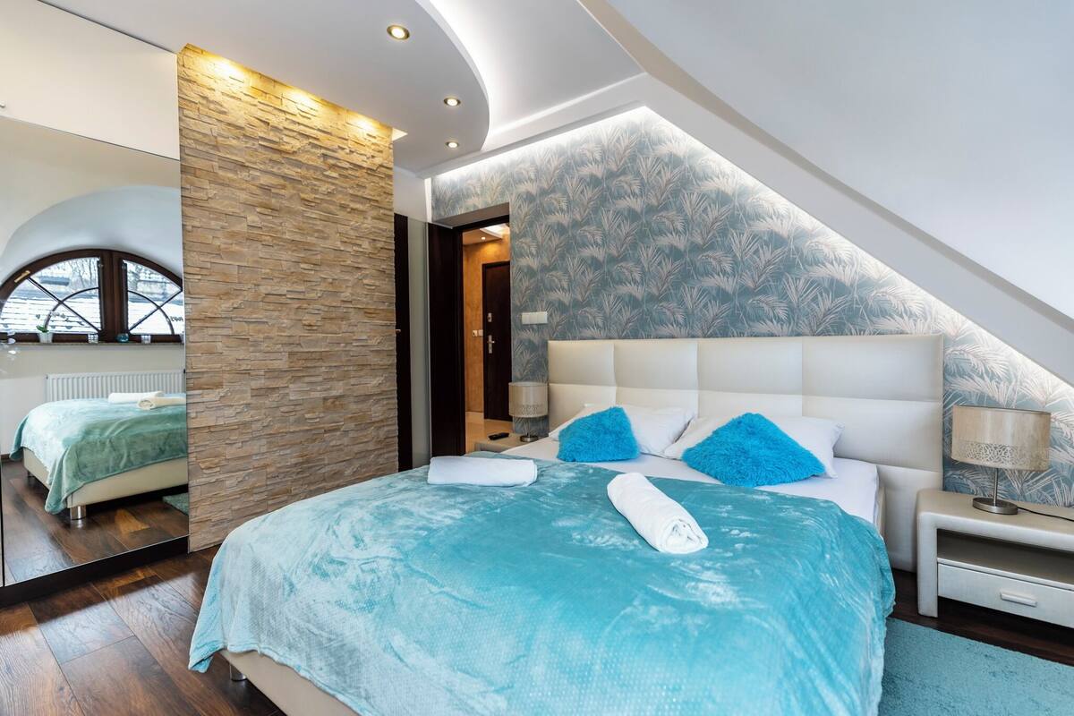 Un dormitorio moderno con una cama grande, una pared de acento de piedra e iluminación empotrada en el techo.