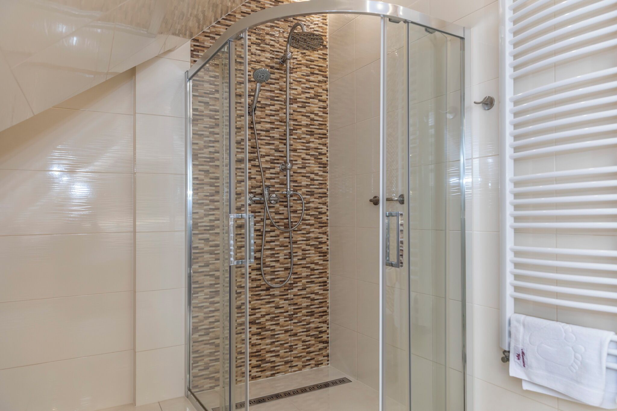 A modern bathroom with a glass shower enclosure, a wooden wall backsplash, and a white towel rack.