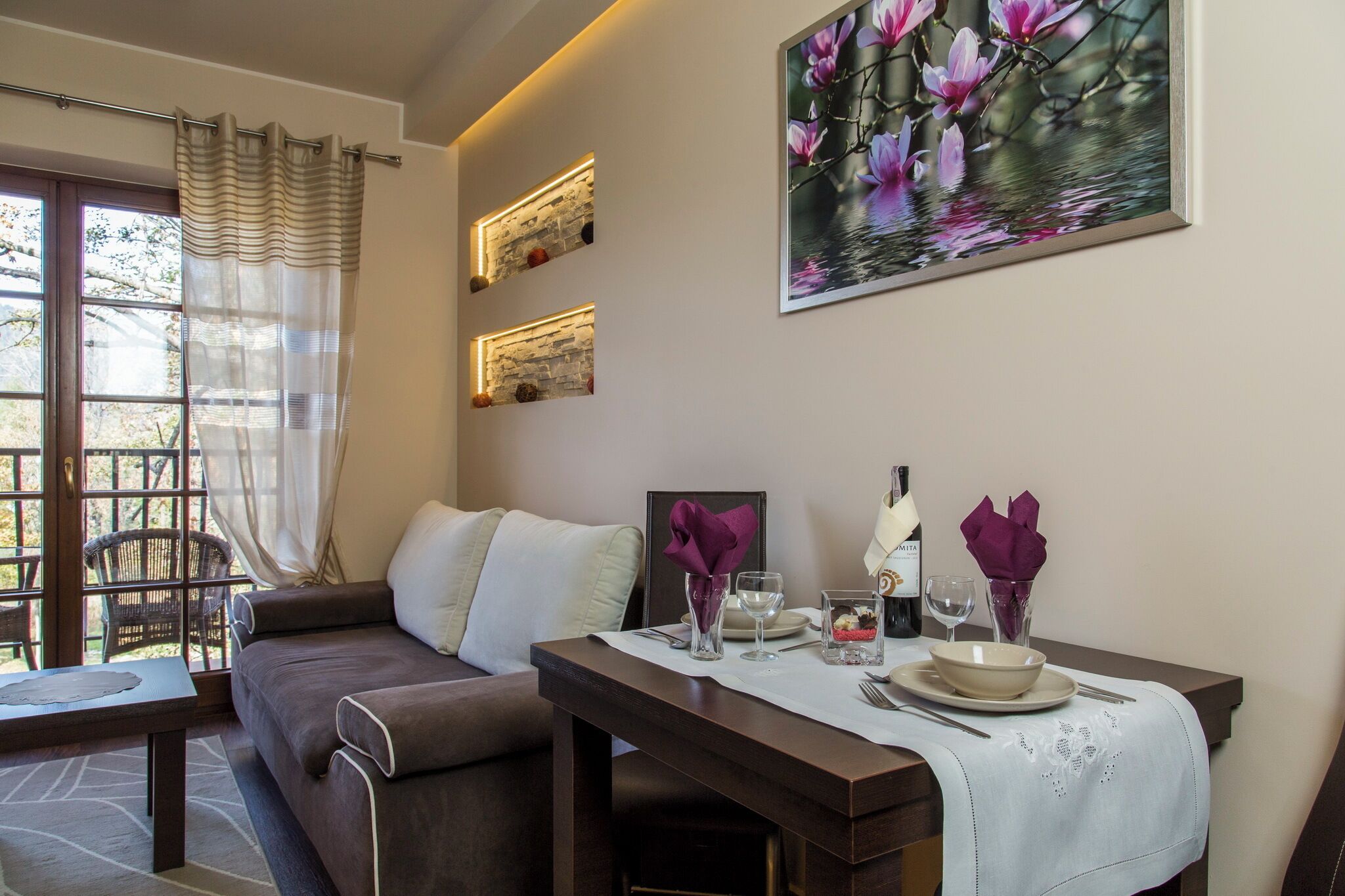 A cozy room with a sofa, a dining table set with plates, glasses, and a vase of flowers.