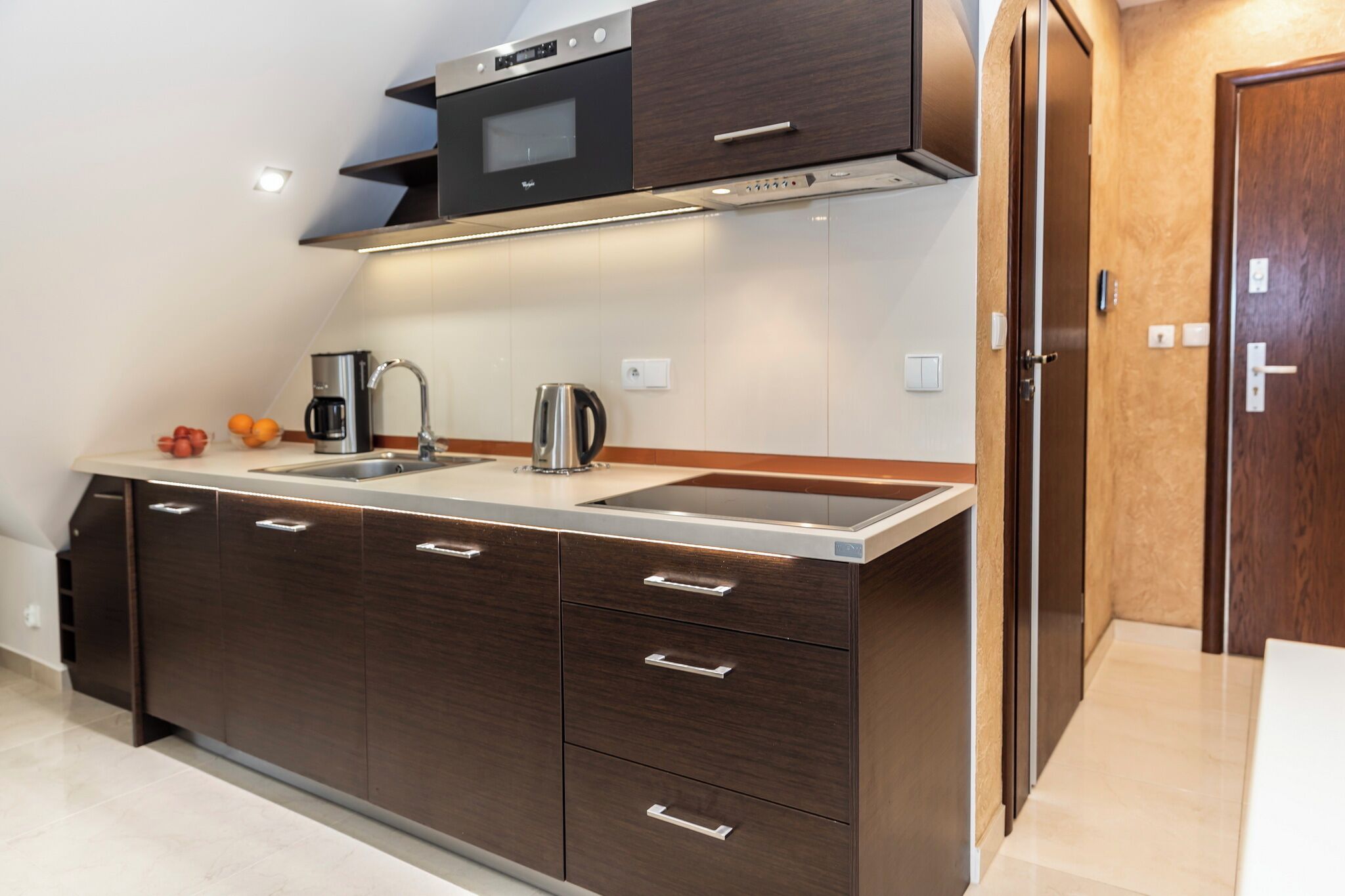 A modern kitchen with dark wooden cabinets, a stainless steel sink, and a built-in microwave.