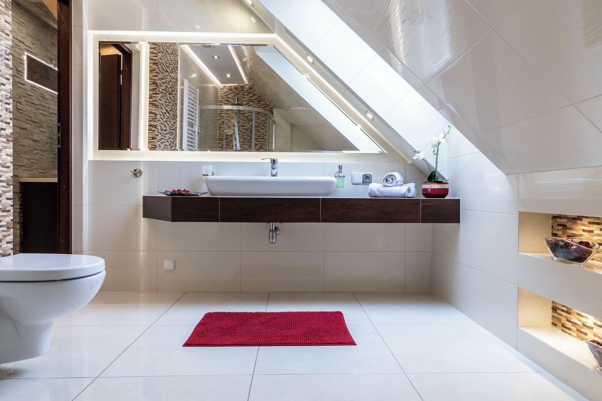 A modern bathroom with a white sink, a mirror above it, and a red rug on the floor.