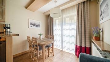 A dining area with a wooden table and chairs, a coffee machine, a potted plant, and a window with curtains.