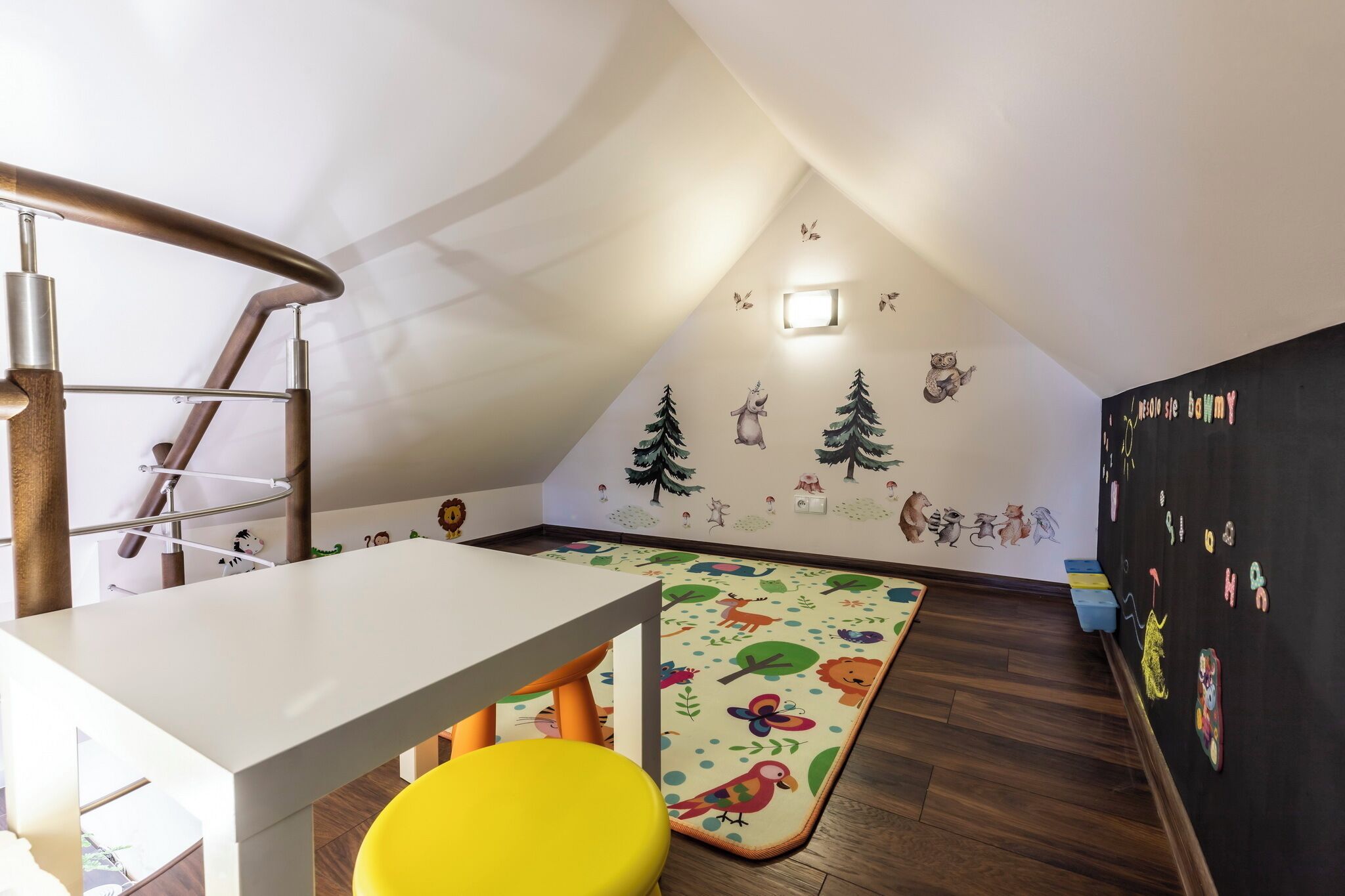 Een kinderkamer met een witte tafel, een gele stoel, een kleurrijk vloerkleed en een muur versierd met dierenstickers.