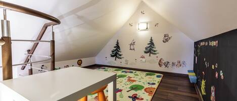 Um quarto infantil com uma mesa branca, uma cadeira amarela, um tapete colorido e uma parede decorada com adesivos de animais.