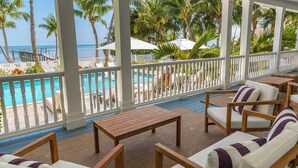 A covered outdoor seating area with a pool view, wooden furniture, and a white railing. - Turtle Crawl on Long Key Oceanfront Beachfront with dock and pool (Long Key)
